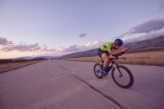 triathlon athlete riding professional racing bike on morning workout sunset or sunrise in background