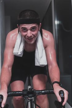 Man cycling on the machine trainer he is exercising in the home at night. Playing online bike racing game during coronavirus covid19 lockdown. New normal concept.