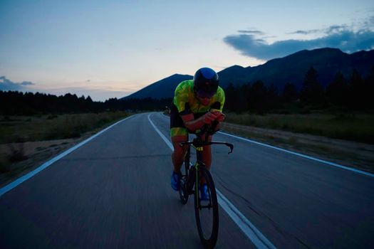 triathlon athlete riding professional racing bike at night workout on curvy country road w