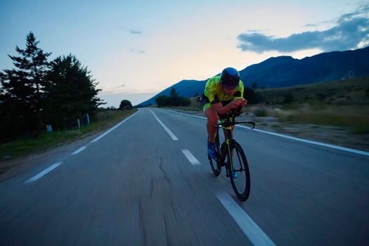 triathlon athlete riding professional racing bike at night workout on curvy country road w