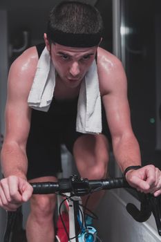 Man cycling on the machine trainer he is exercising in the home at night. Playing online bike racing game during coronavirus covid19 lockdown. New normal concept.