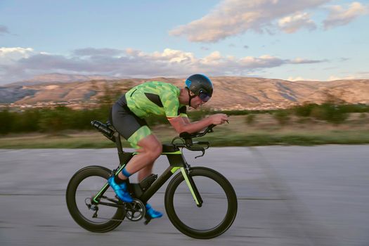 triathlon athlete riding professional racing bike on morning workout sunset or sunrise in background