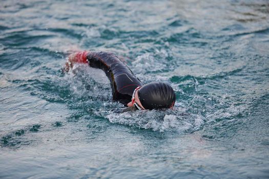 triathlon athlete swimming on beautiful morning sunrise training in lake wearing wetsuit concept of strength and endurance