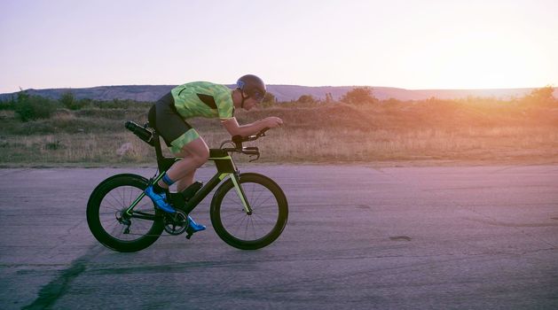 triathlon athlete riding professional racing bike on morning workout sunset or sunrise in background