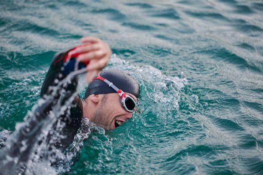 triathlon athlete swimming on beautiful morning sunrise training in lake wearing wetsuit concept of strength and endurance