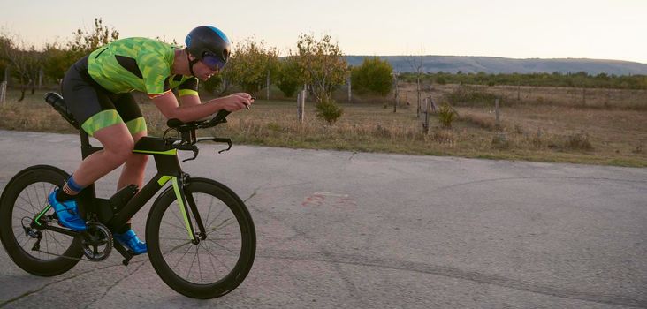 triathlon athlete riding professional racing bike on morning workout sunset or sunrise in background