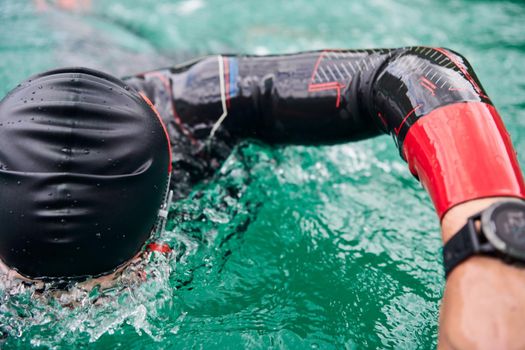 triathlon athlete swimming on extreme morning training in green lake wearing wetsuit