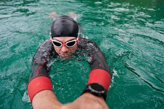 triathlon athlete swimming on extreme morning training in green lake wearing wetsuit