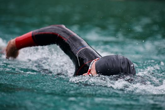 triathlon athlete swimming on extreme morning training in green lake wearing wetsuit