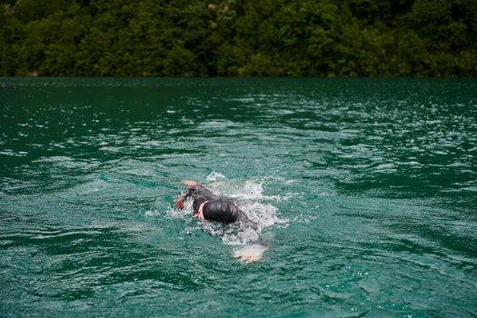 triathlon athlete swimming on extreme morning training in green lake wearing wetsuit