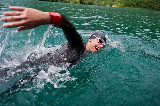 triathlon athlete swimming on extreme morning training in green lake wearing wetsuit