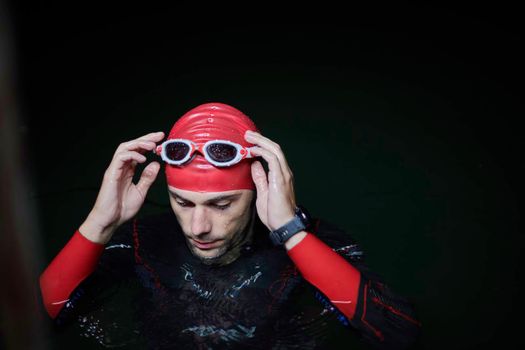real triathlete swimmer having a break during hard training at lake on dark night