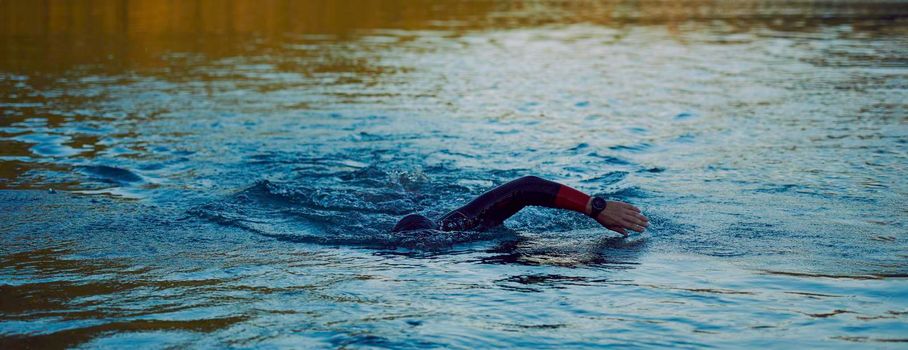 triathlon athlete swimming on beautiful morning sunrise training in lake wearing wetsuit concept of strength and endurance