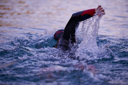 triathlon athlete swimming on beautiful morning sunrise training in lake wearing wetsuit concept of strength and endurance