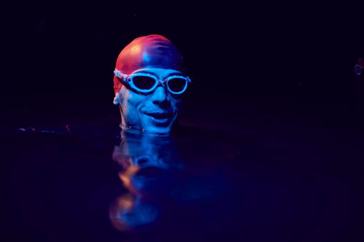 real triathlete swimmer having a break during hard training at lake on dark night neon gel color lights