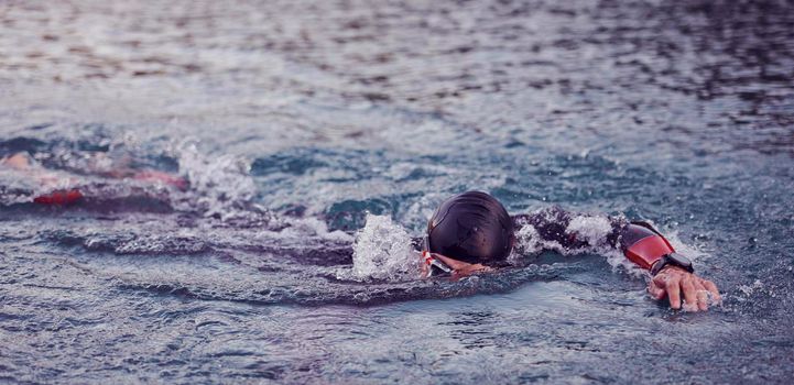 triathlon athlete swimming on beautiful morning sunrise training in lake wearing wetsuit concept of strength and endurance