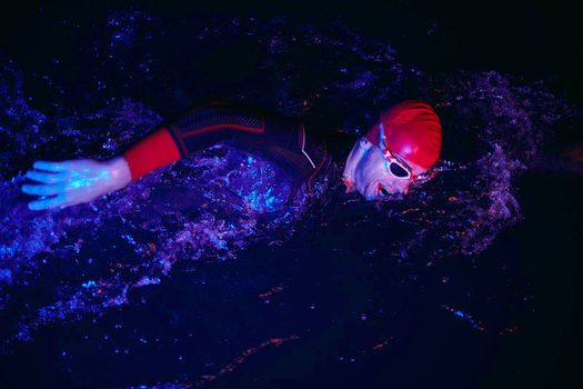 authentic triathlon swimmer have extreme training  on dark night wearing wetsuit neon gel color lights