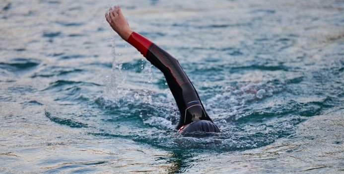 triathlon athlete swimming on beautiful morning sunrise training in lake wearing wetsuit concept of strength and endurance