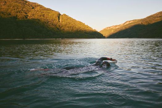 triathlon athlete swimming on beautiful morning sunrise training in lake wearing wetsuit concept of strength and endurance