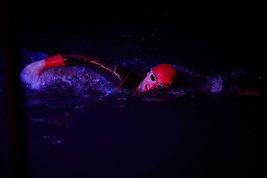 authentic triathlon swimmer have extreme training  on dark night wearing wetsuit neon gel color lights