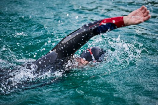 triathlon athlete swimming on beautiful morning sunrise training in lake wearing wetsuit concept of strength and endurance