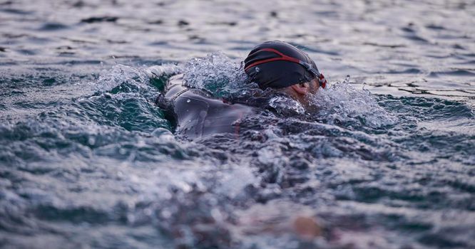 triathlon athlete swimming on beautiful morning sunrise training in lake wearing wetsuit concept of strength and endurance