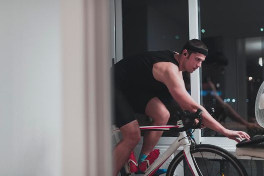 Man cycling on the machine trainer he is exercising in the home at night. Playing online bike racing game during coronavirus covid19 lockdown. New normal concept.