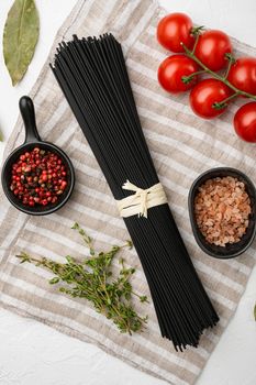 Black dry raw noodles spaghetti pasta set, on white stone table background, top view flat lay