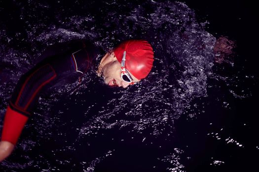 triathlon swimmer have extreme training  on dark night wearing wetsuit concept of strength and endurance