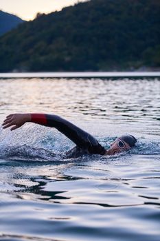 triathlon athlete swimming on beautiful morning sunrise training in lake wearing wetsuit concept of strength and endurance