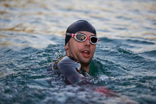 real triathlete swimmer having a break during hard training at lake on beautiful morning