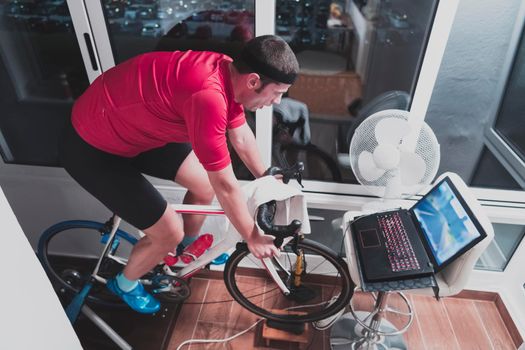 Man cycling on the machine trainer he is exercising in the home at night. Playing online bike racing game during coronavirus covid19 lockdown. New normal concept.