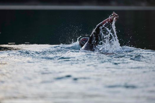 triathlon athlete swimming on beautiful morning sunrise training in lake wearing wetsuit concept of strength and endurance