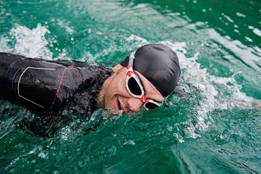 triathlon athlete swimming on extreme morning training in green lake wearing wetsuit