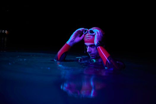 real triathlete swimmer having a break during hard training at lake on dark night neon gel color lights