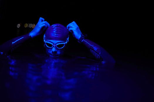 real triathlete swimmer having a break during hard training at lake on dark night neon gel color lights