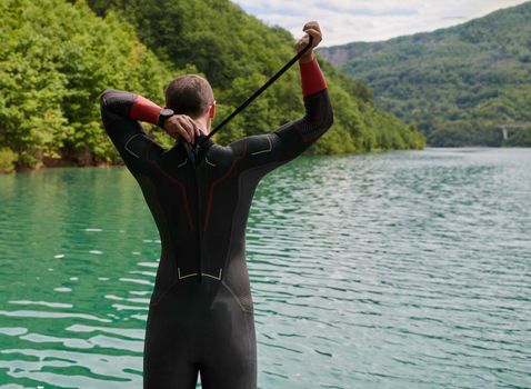 triathlon athlete getting ready and prepare goggles hat and  wetsuit for swimming training on lake