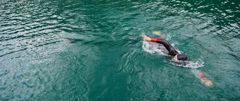 triathlon athlete swimming on extreme morning training in green lake wearing wetsuit