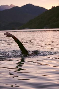 triathlon athlete swimming on beautiful morning sunrise training in lake wearing wetsuit concept of strength and endurance