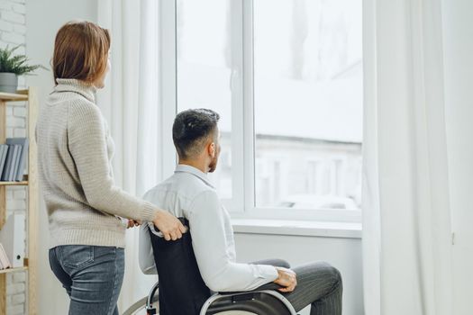 Woman caring for disabled man in wheelchair at home close up
