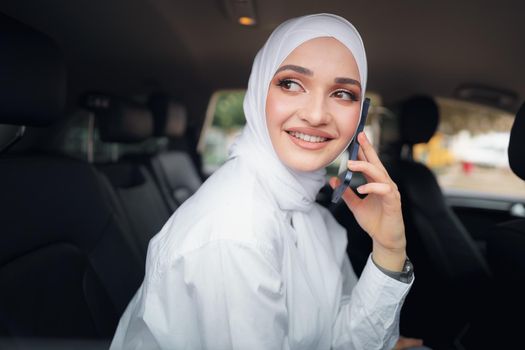 Beautiful young woman in hijab sitting in a car and talking on the phone, close up