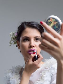 bride paints lips with lipstick on their wedding day in dress isolated on a white background