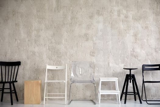 Wooden plastic and metal chairs placed in row near cement wall in studio. Different types configurations and materials of chair