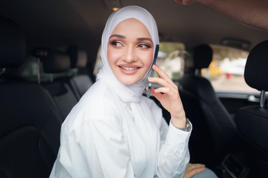 Beautiful young woman in hijab sitting in a car and talking on the phone, close up