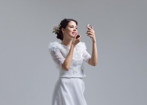 bride paints lips with lipstick on their wedding day in dress isolated on a white background