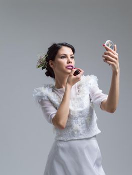 bride paints lips with lipstick on their wedding day in dress isolated on a white background