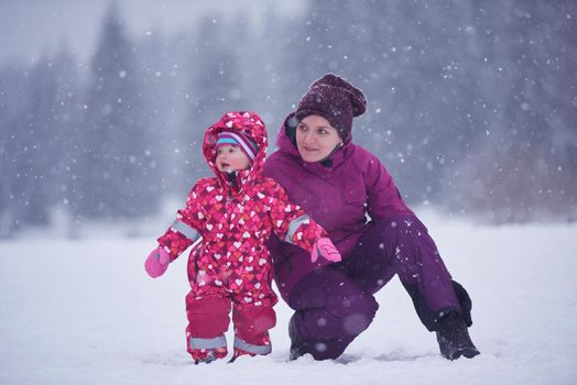 happy family on winter vacation, mom and cute little girl have fun and slide while snow falkes falling