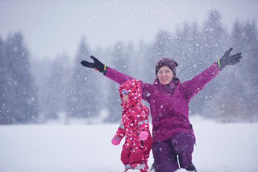 happy family on winter vacation, mom and cute little girl have fun and slide while snow falkes falling