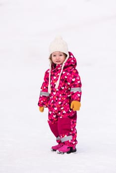 happy cute little girl wearing a red snow suit and white hat  while having fun and playing on fresh snow at snowy winter day