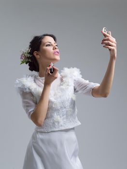 bride paints lips with lipstick on their wedding day in dress isolated on a white background